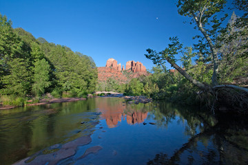 Cathedral Rock reflected in Oak Creek amidst green summer foliage near Sedona, Arizona on cloudless summer afternoon.