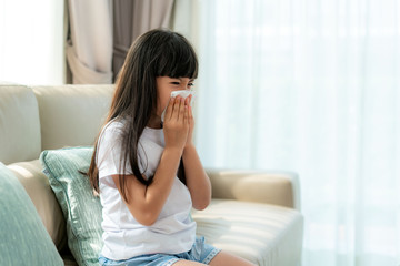 Asian child or kid girl sick and sad with sneezing on nose and cold cough on tissue paper because...