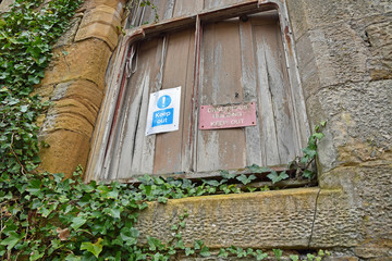 Keep out dangerous building signs on boarded up window with climbing ivy surrounding. Crawford Priory, Cupar, Fife, Scotland: an abandoned, derelict gothic mansion.