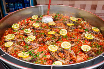 Large round pot with fish sour soup known as borscht with red tomatoes, decorated with fresh yellow lemon slices, ready to eat healthy traditional East European food or seafood