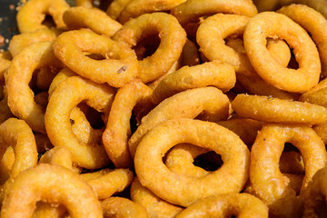 Large group of freshly fried calamari and onion rings on display for sale at a street food festival, ready to eat healthy seafood, beautiful orange monochrome outdoor background