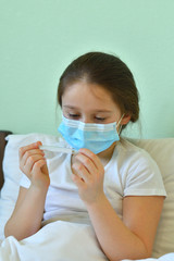 girl looks at a high-temperature thermometer.Quarantine.Blue infection preventive face mask . I virus infection in Corona virus crisis 2020. Take care kids from infection.