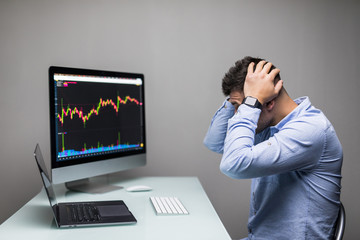 Sad Businessman lamenting with hands on the head in front of computer with graph of unsuccessful business on the screen.