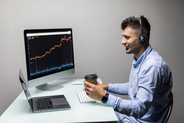 Side view of male trader with coffee cup using multiple computer screens while communicating through headphones at desk