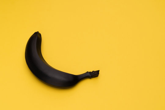 Matte black banana on the yellow background. The object is at the left side of the picture. Minimal style. Conceptual minimalism. Matte surface. Fruit. One. Copy space