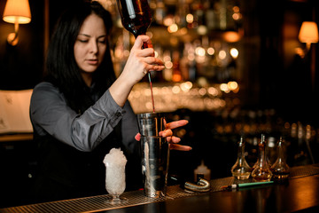 Woman bartender pours alcoholic drink from bottle into shaker.