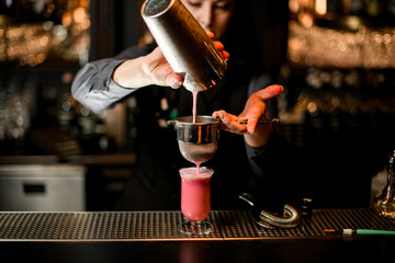 Fototapeta na wymiar bartender carefully pours cocktail from shaker into glass using sieve.
