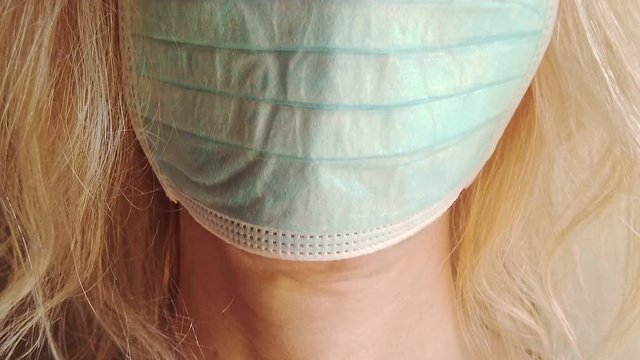 front view closeup of a blonde girl with a sanitary mask on white background isolated. Concept of the epidemic outbreak, quarantine for public health care and outbreak of the corona-virus. SLOW MOTION