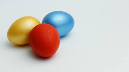 three colored Easter eggs blue red and gold close up on a white background