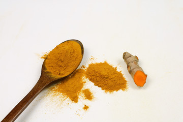 Turmeric powder in a wooden spoon and fresh turmeric roots isolated on a white background is an ingredient in turmeric foods and ingredients in skin care products. Turmeric helps strengthen the skin.