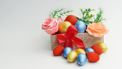 Easter eggs of large sizes and bright colors are in a beautiful box with flowers and small colored eggs are freely lying near the box