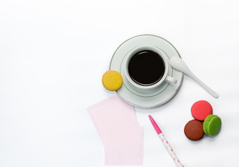 cup with coffee and macrons, pen and note paper.