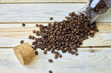 scattered coffee beans from glass bottle and cork on a wooden table