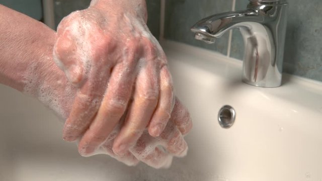 SLOW MOTION, CLOSE UP, DOF: Aging man is washing his hands to avoid getting infected by the widespread corona virus. Unrecognizable person thoroughly washes their hands with antibacterial soap.