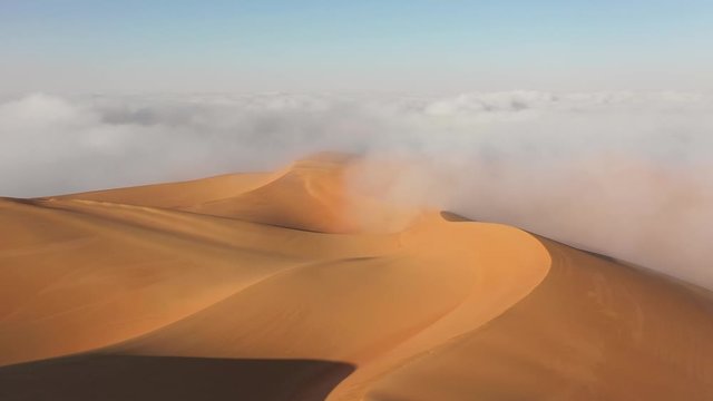 Aerial view from a drone flying low over massive sand dunes surrounded by fog. Liwa desert, Abu Dhabi, United Arab Emirates.