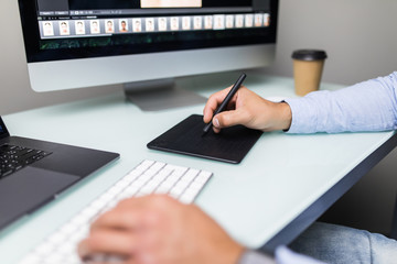 Hand of male designer working at his desk using stylus and digital graphics tablet.