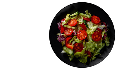 various fresh mix salad leaves with tomato, cucumber and red pepper on a black plate isolated on white background. with copy space. top view