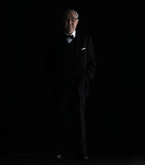 old man in a black suit on a black studio background