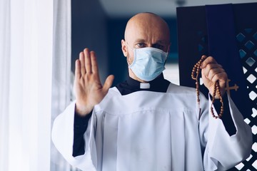 Man priest in medical mask praying with cross and rosary.