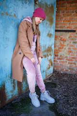 stylish girl model in a brown coat, pink suit and gray boots on the city ruins. The trends of...
