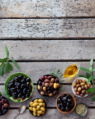Assortment of fresh olives on a plate with olive tree brunches. Wooden background. Copy space. Top view.