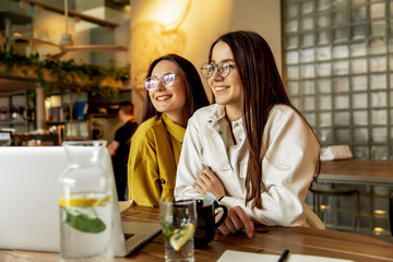 Cheerful young ladies hugging each other at local cafe