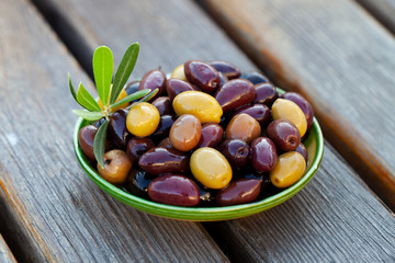 Assortment of fresh olives on a plate with olive tree brunches. Wooden background. Close up.