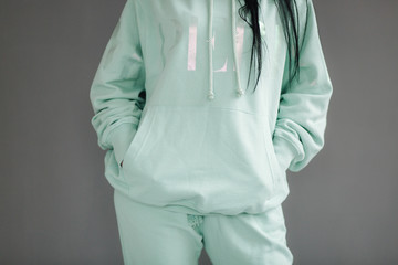 Attractive young model in tracksuit. Woman demonstrating clothes in studio. Gray background