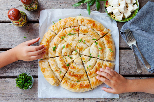 Traditional spiral shape phyllo pastry pie, banitsa with kids hands holding. Wooden background. Top view.