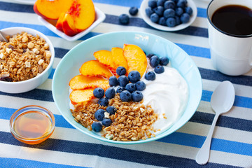 Healthy breakfast, muesli, granola with yogurt, fruits and berries in blue bowl. Stripped textile background.