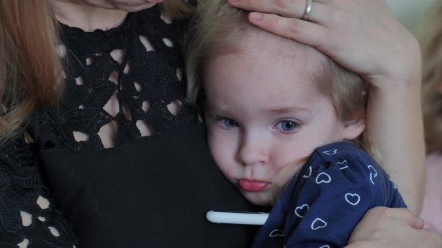 Caring mother in a bandage measures her daughter's temperature.