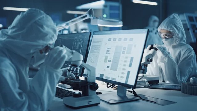 Research Factory Cleanroom: Engineers / Scientists wearing Coveralls and Gloves Use Microscopes to Inspect Motherboard Microprocessor Components, Developing High Tech Modern Electronics