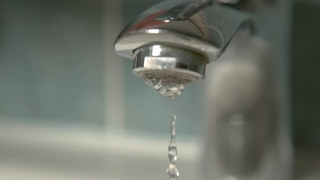 Slow motion, macro, DOF crystal clear water stops flowing from a shiny metal bathroom faucet