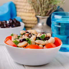 Traditional greek white bean salad with olives in a plate on a business wooden table.