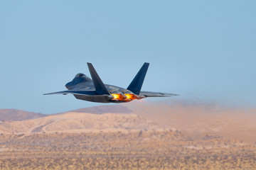 Very low pass of a F-22 Raptor against the Nevada hills, with afterburners on and  
the jet stream visible behind the aircraft
 - obrazy, fototapety, plakaty