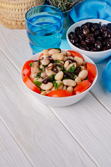 Traditional greek white bean salad with olives in a plate on a business wooden table.