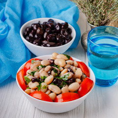 Traditional greek white bean salad with olives in a plate on a business wooden table.