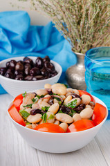 Traditional greek white bean salad with olives in a plate on a business wooden table.