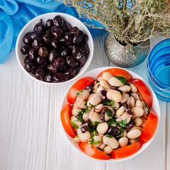 Traditional greek white bean salad with olives in a plate on a business wooden table.