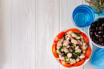 Traditional greek white bean salad with olives in a plate on a business wooden table.