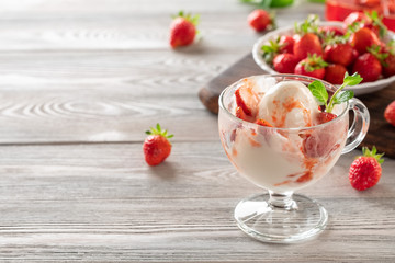 Tasty creamy ice cream with stawberry, poured with sweet syrup in a glass cup on a light background