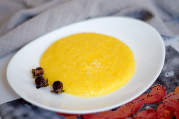 A portion of corn porridge with a piece of butter on a white plate decorated with frozen berries. C lose- up, selective focus, blur.