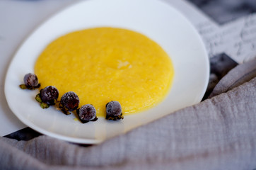 A portion of corn porridge with a piece of butter on a white plate decorated with frozen berries. C lose- up, selective focus, blur.