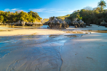 Small beach between rocks at low tide on sunny day with blue sky