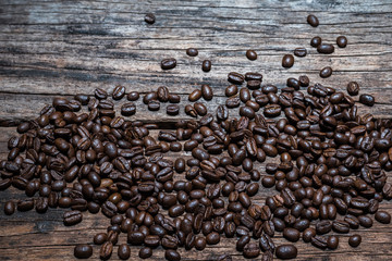 Roasted coffee beans scattered on rustic wooden board.