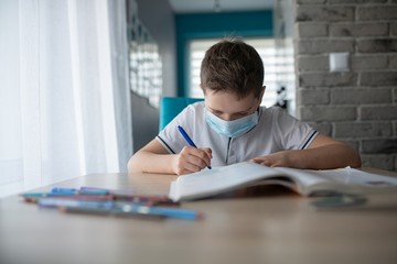 Child in protective medical mask doing his homework. School closed during coronavirus