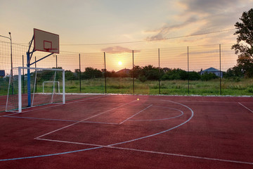 Outdoors mini football and basketball court with ball gate and basket surrounded with high protective fence.