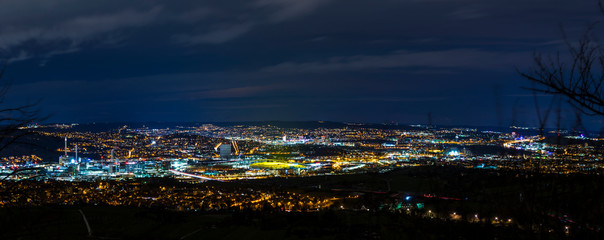 Germany, XXL panorama aerial view above lights of big city stuttgart at night with view on industry, stadium, houses, highway and downtown