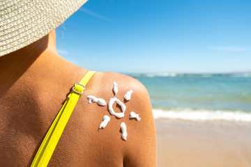Back view of young woman tanning at the beach with sunscreen cream in sun shape on her shoulder. UV...