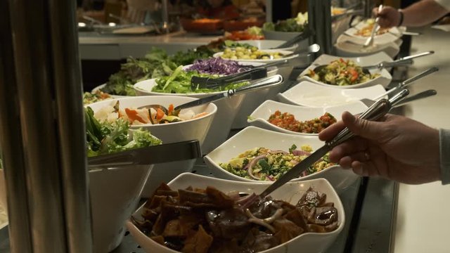 Buffet table at the restaurant. Hot and fresh food at a mall food court. Self service meals. Woman hand takes salad from smorgasbord table 4k